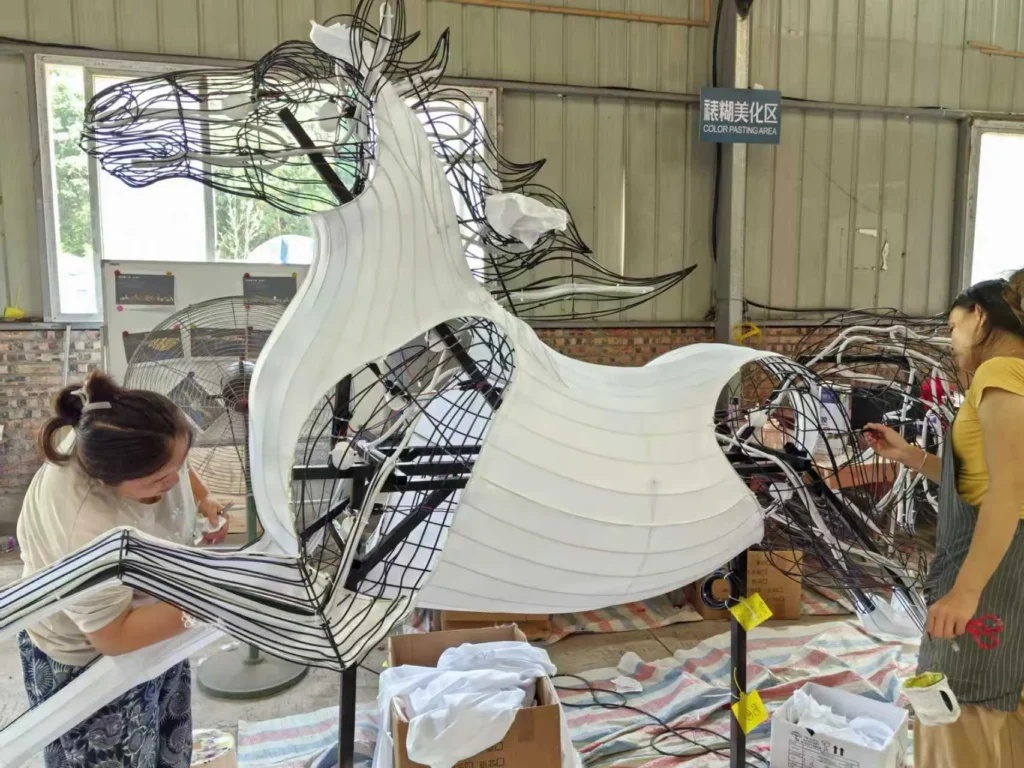Workers fit white fabric over a horse frame, with open areas showing the underlying ribs and curves.