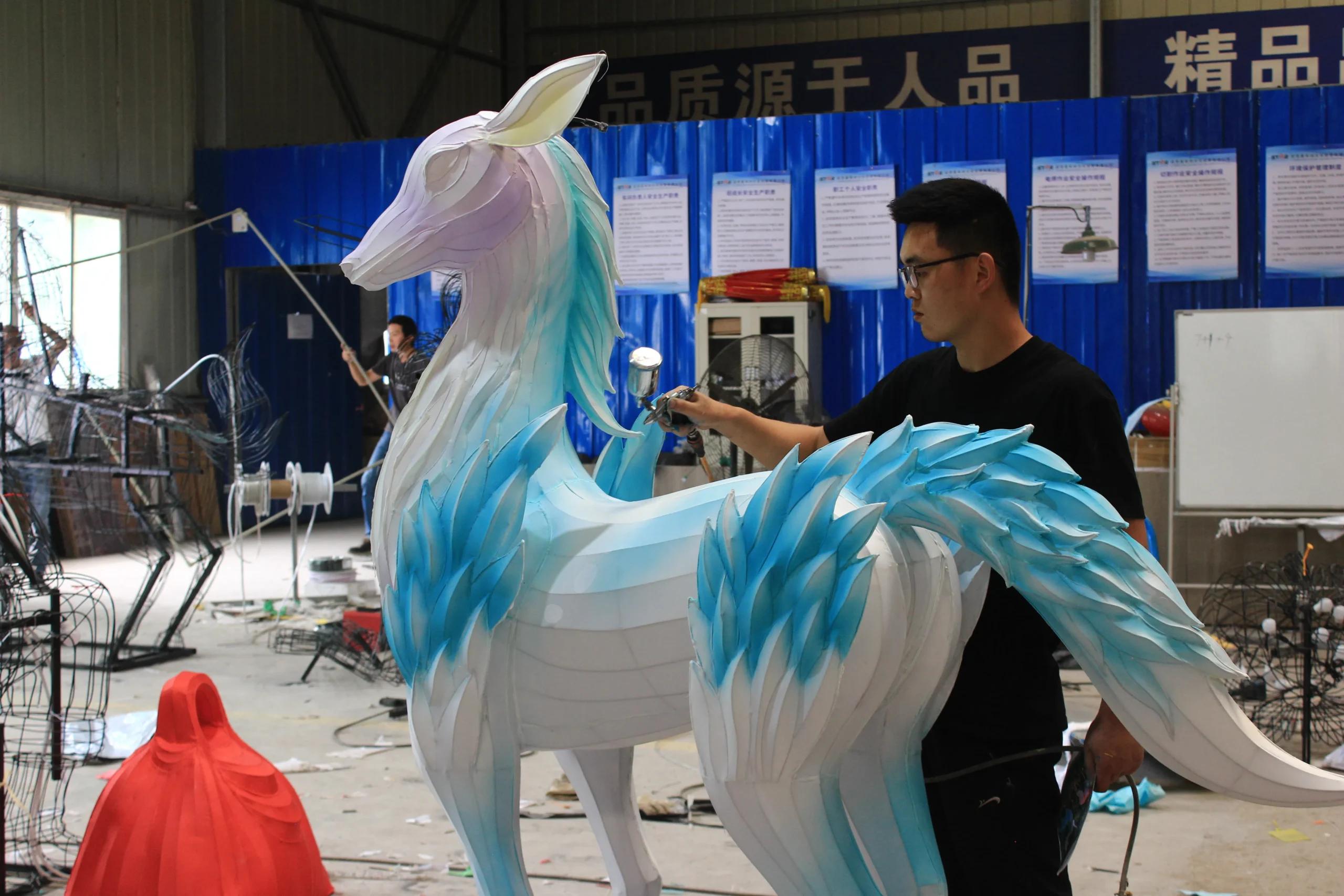 An artist uses a spray gun to apply blue colour to a fabric-covered deer figure.