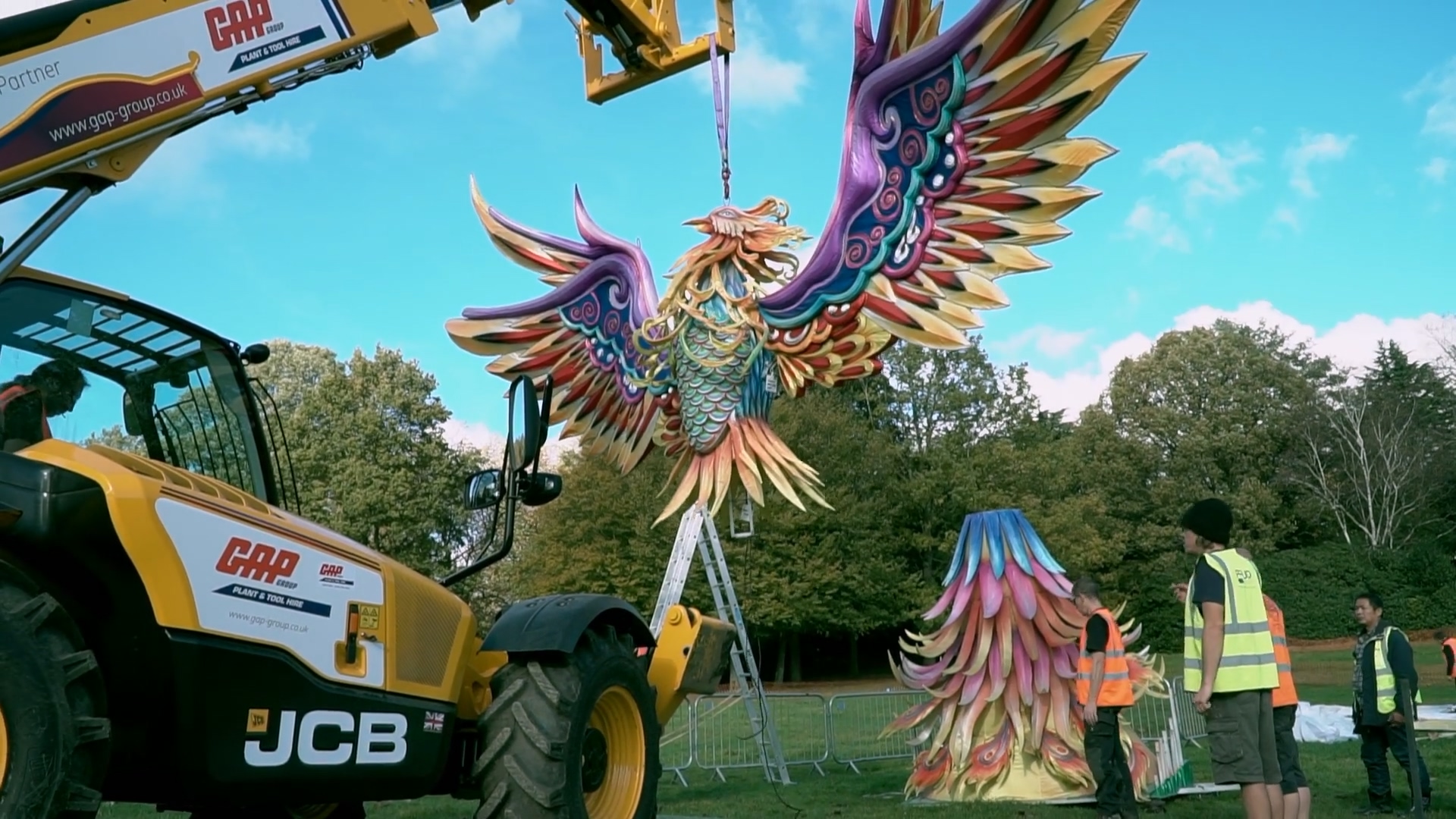 A large phoenix figure is lifted outdoors, with crew, handling equipment and display sections visible.