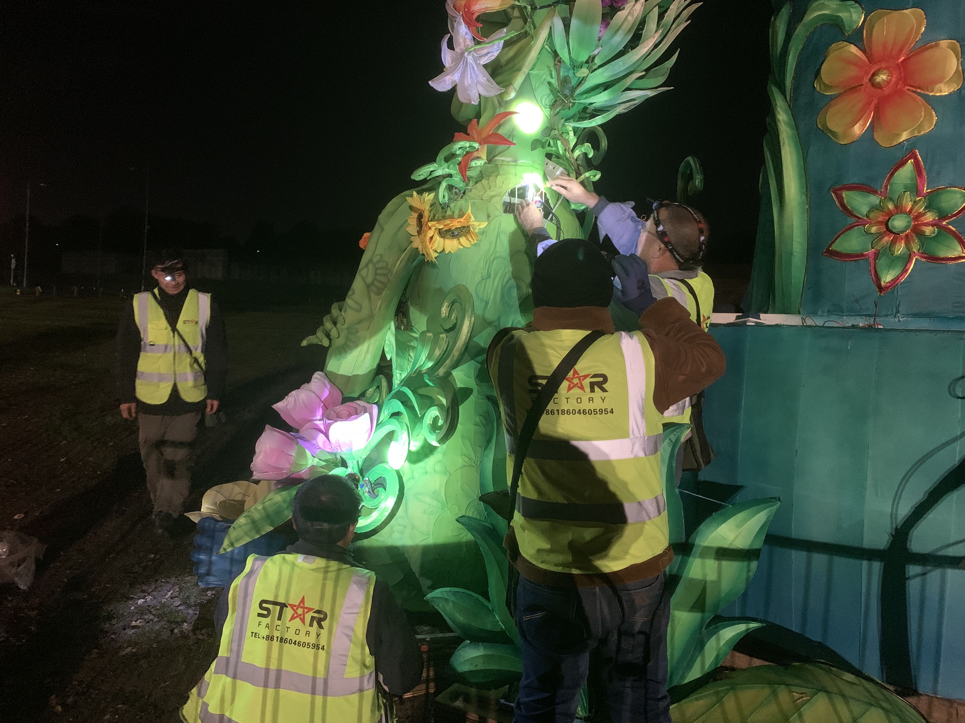Crew members work on a floral figure at night in an illuminated display.